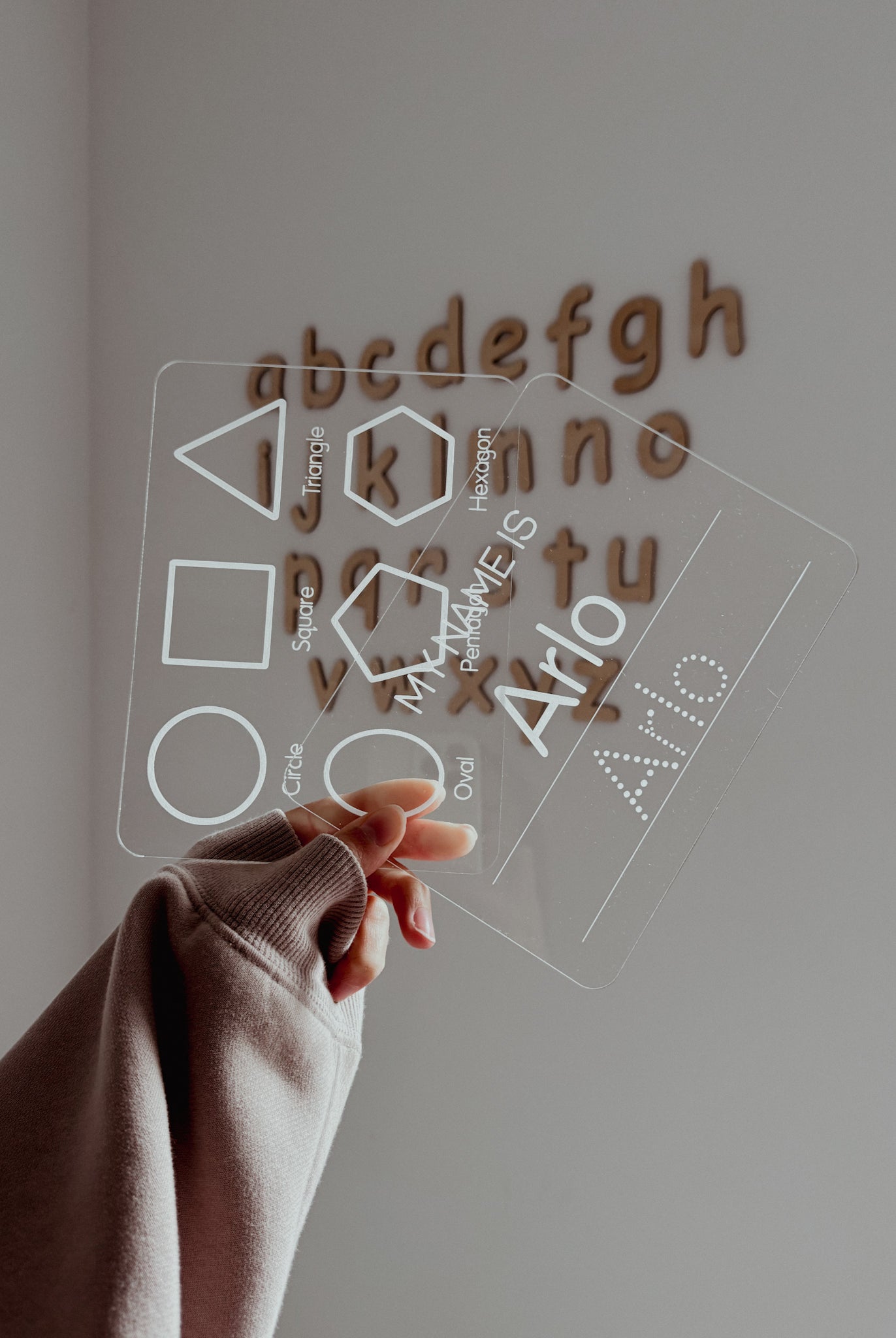 Hand interacting with a transparent board with letter and shape cutouts on a plain background
