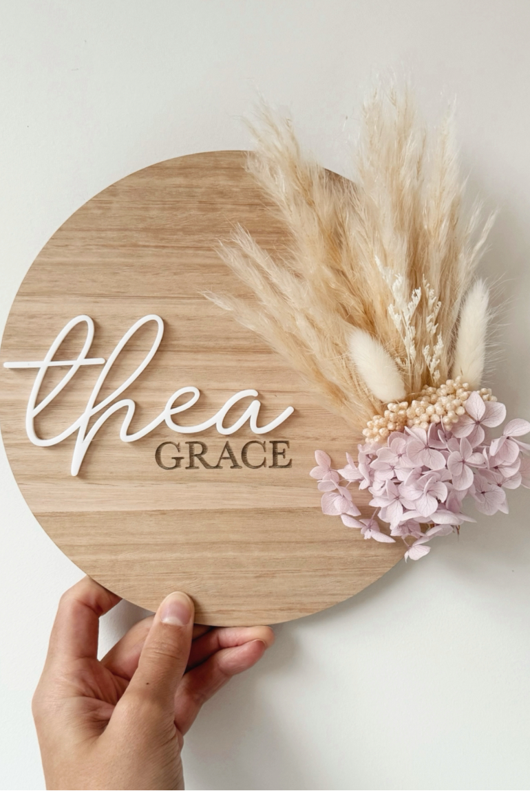 Dried floral wooden plaque with acrylic and/or laser engraved text or name, either arch or round shape, with dried preserved flowers tied to the plaque. Perfect for baby birth announcements or personalised gifts or keepsakes.