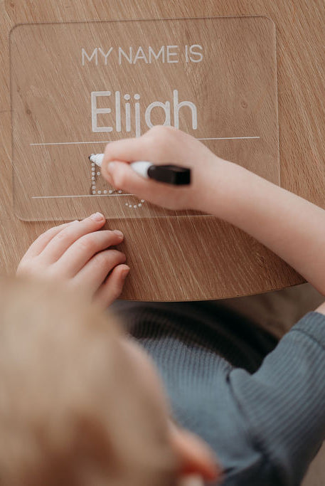 kid writing 'My Name is' on a acrylic board with a marker.
