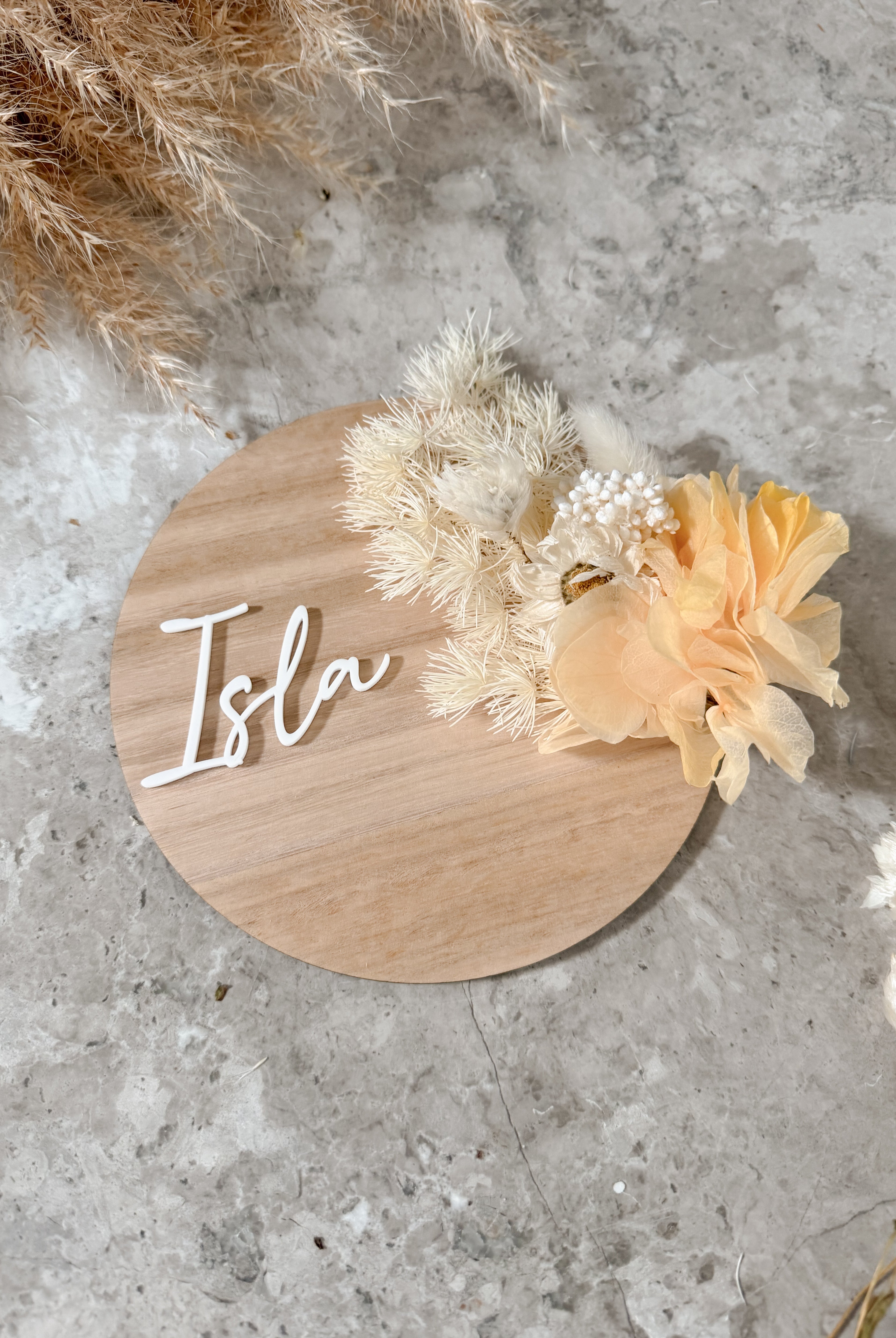 Dried floral wooden plaque with acrylic and/or laser engraved text or name, either arch or round shape, with dried preserved flowers tied to the plaque. Perfect for baby birth announcements or personalised gifts or keepsakes.