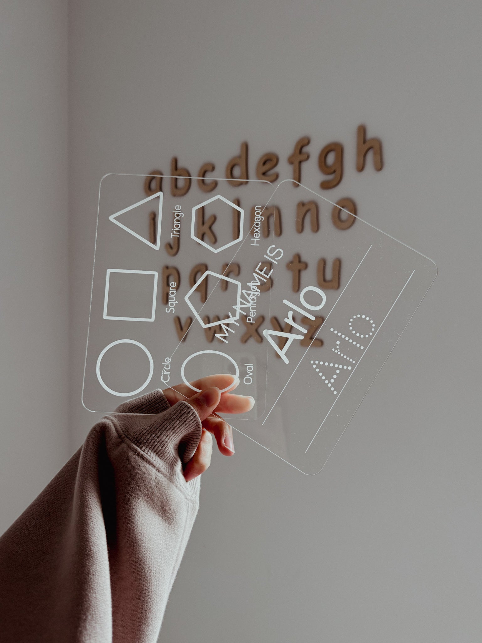 Hand interacting with a transparent board with letter and shape cutouts on a plain background