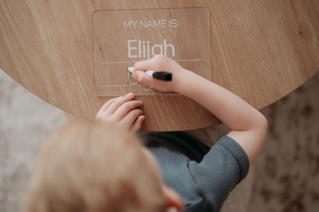 kid writing 'My Name is' on a acrylic board with a marker.