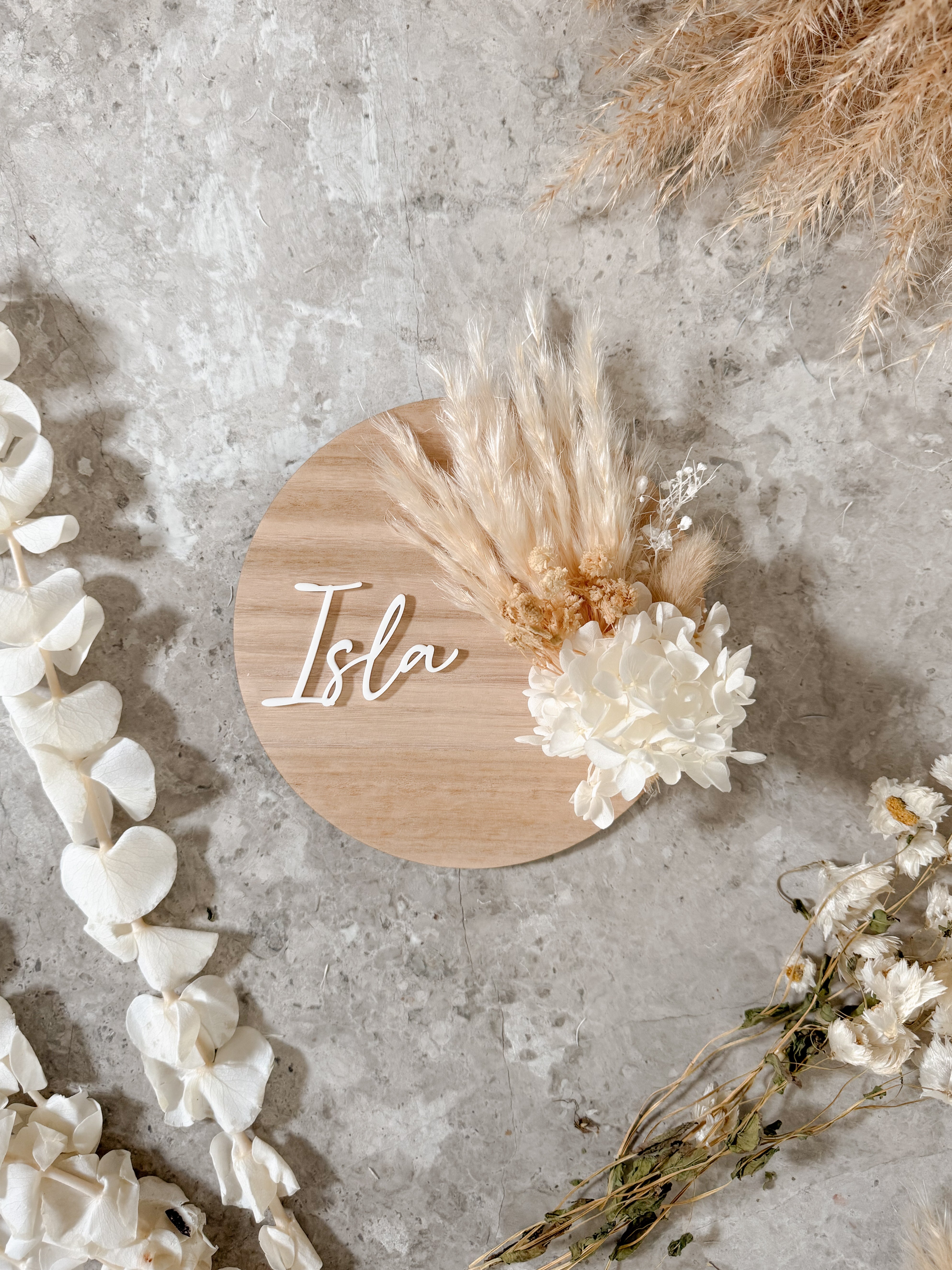 Dried floral wooden plaque with acrylic and/or laser engraved text or name, either arch or round shape, with dried preserved flowers tied to the plaque. Perfect for baby birth announcements or personalised gifts or keepsakes.