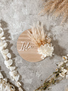 Dried floral wooden plaque with acrylic and/or laser engraved text or name, either arch or round shape, with dried preserved flowers tied to the plaque. Perfect for baby birth announcements or personalised gifts or keepsakes.